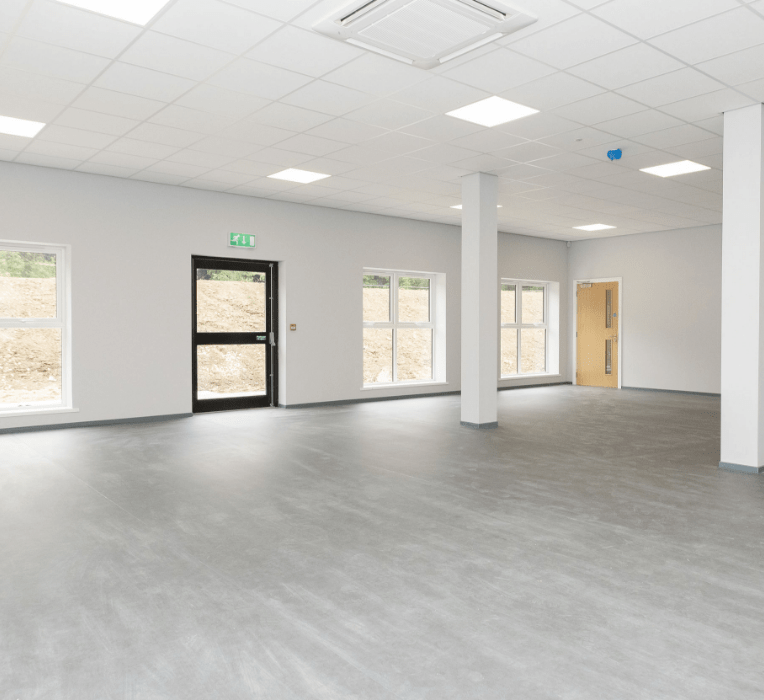 A spacious, empty room with windows, columns, and a black exit door with a green 